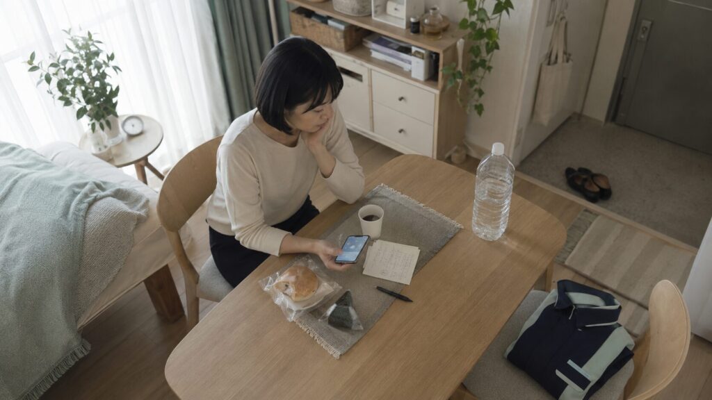 コンビニの商品で朝食をとりながら、天気と商品の売れ行きを確認する出勤前の女性。